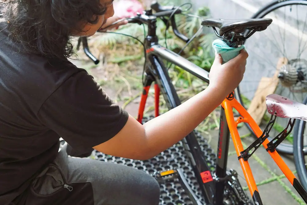 A person wiping down the frame of an orange and black bicycle outdoors