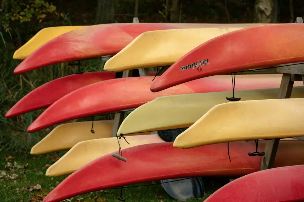 Several colorful kayaks resting upside down on a wooden storage rack outdoors