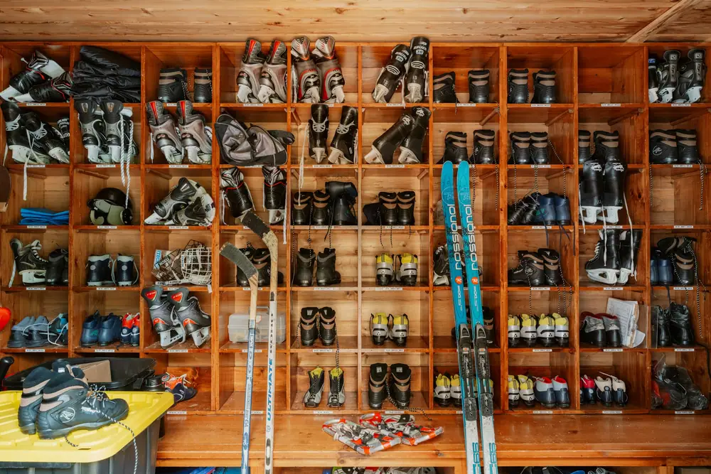 Rows of ski boots on wooden shelves with skis leaning against the wall
