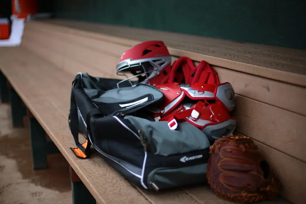 A sports bag, catcher helmet and baseball glove sitting on a dugout bench